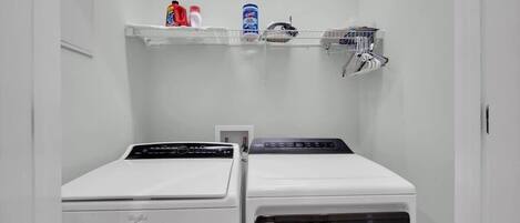 A laundry area with two washing machines and a shelf with cleaning supplies.