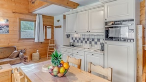 Interior acogedor de una cabaña con una mesa de comedor de madera, un frutero, un sofá y una cocina con armarios blancos y salpicadero de azulejos.