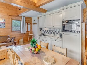 A cozy cabin interior with a wooden dining table, a fruit bowl, a sofa, and a kitchen area with white cabinets and a tiled backsplash. - Comfortable duplex 6 pers, WIFI, private garage in Champagny (Champagny-en-Vanoise)