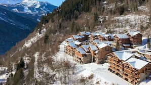 Un conjunto de cabañas de madera con techos nevados, frente a un telón de fondo de montañas nevadas y un bosque denso.