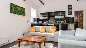 Una sala de estar moderna con un sofá gris, una mesa de centro de madera y una cocina al fondo.