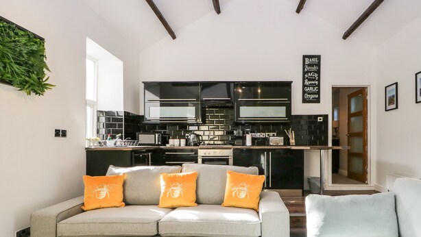 Una sala moderna con un sofá gris, una mesa de centro de madera y una cocina al fondo.