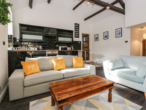 A modern living room with a grey sofa, a wooden coffee table, and a kitchen in the background.