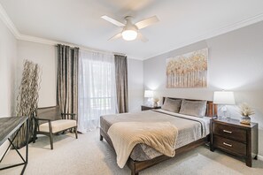 A bedroom with a bed, bedside tables, a desk, a chair, a ceiling fan, and a window with curtains. - Montrose Houston's Urban Charm (Houston)