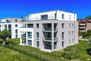 A modern multi-story residential building with balconies, large windows, and a flat roof.