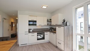 A modern kitchen with white cabinets, a built-in oven, and a large window providing natural light.
