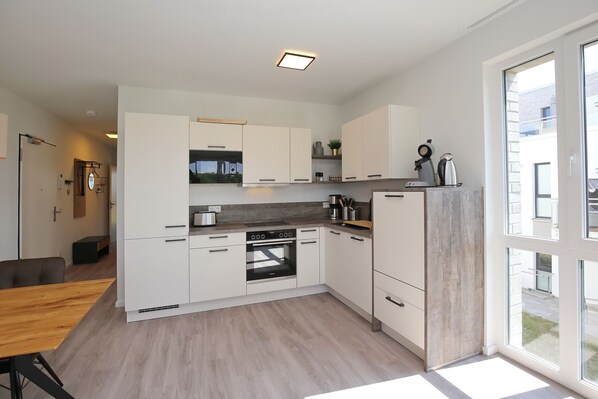 A modern kitchen with white cabinets, a built-in oven, and a large window providing natural light.