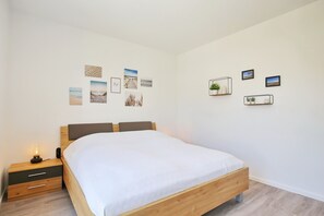 A bedroom with a wooden bed, a nightstand with a lamp, and wall-mounted shelves with plants. - Weiße Villen Wohnung 15 (Ostseebad Boltenhagen)