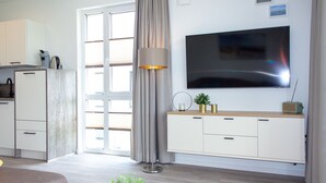 A modern living room with a flat-screen TV, a sofa, a coffee table, a lamp, and a small plant.