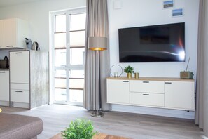 A modern living room with a flat-screen TV, a sofa, a coffee table, a lamp, and a small plant.