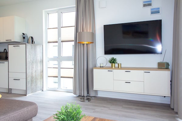 A modern living room with a flat-screen TV, a sofa, a coffee table, a lamp, and a small plant.