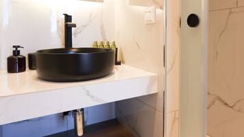 A modern bathroom with a black vessel sink, white marble countertop, and a glass shower enclosure.