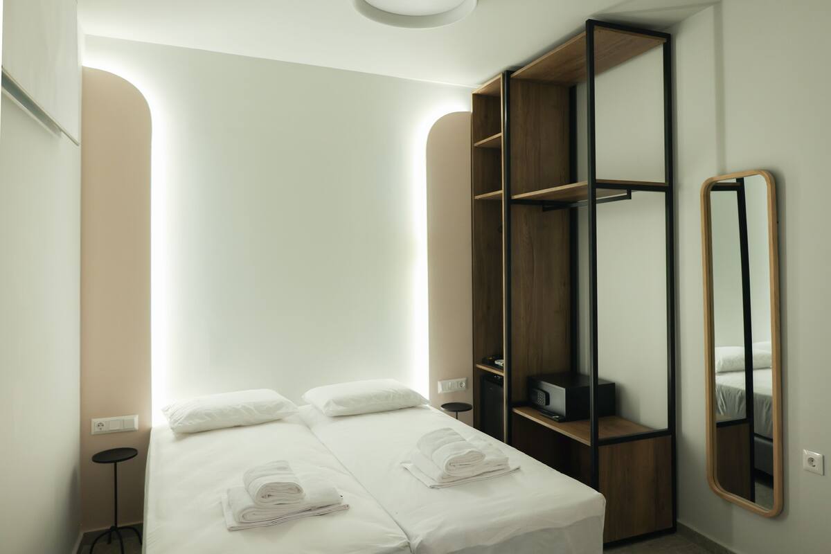 Een hotelkamer met een bed, twee nachtkastjes, een kledingkast, een spiegel en een wandlamp.