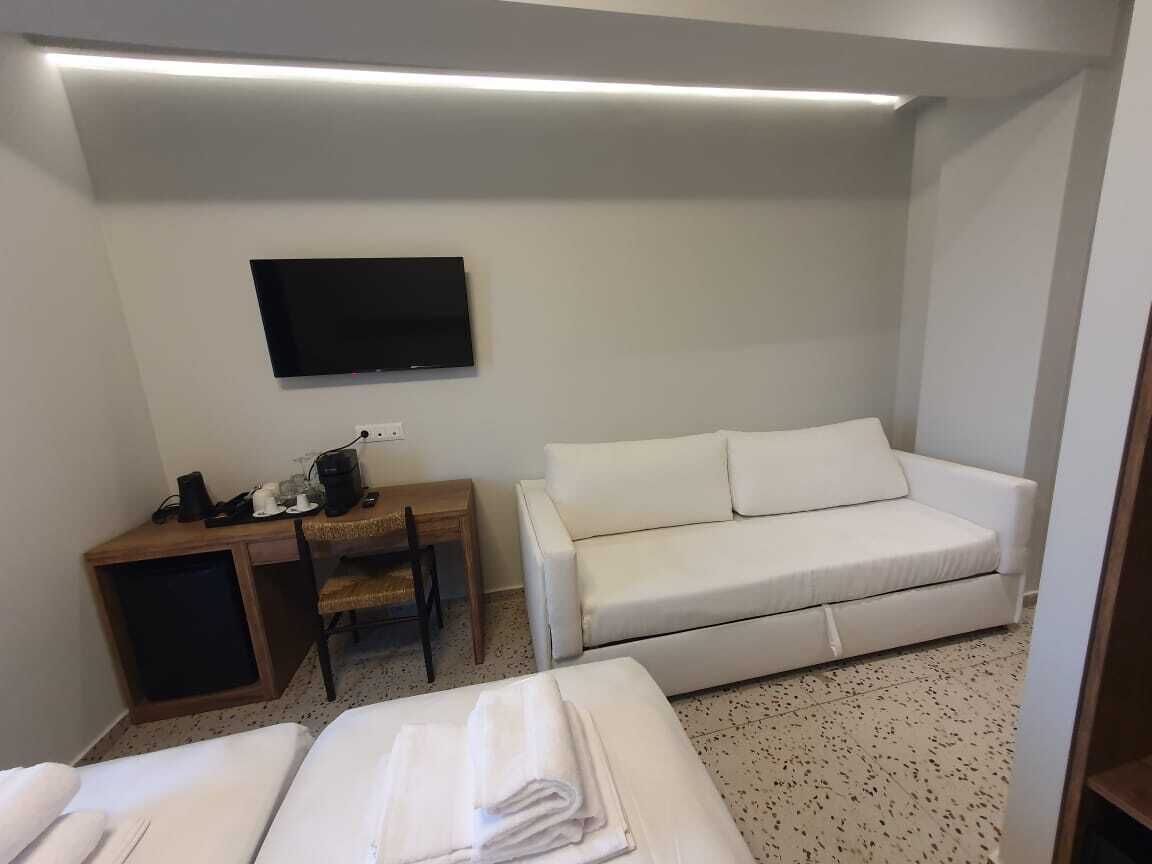 Une chambre d’hôtel équipée d’un lit, d’un canapé, d’un bureau avec une chaise et d’un téléviseur à écran plat fixé au mur.