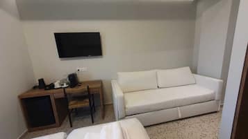 Une chambre d’hôtel équipée d’un lit, d’un canapé, d’un bureau avec une chaise et d’un téléviseur à écran plat fixé au mur.