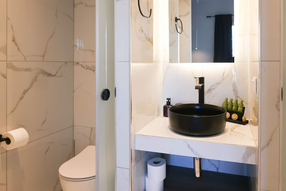 Een badkamer met een wit toilet, een zwart wastafelmeubel en een spiegel erboven.