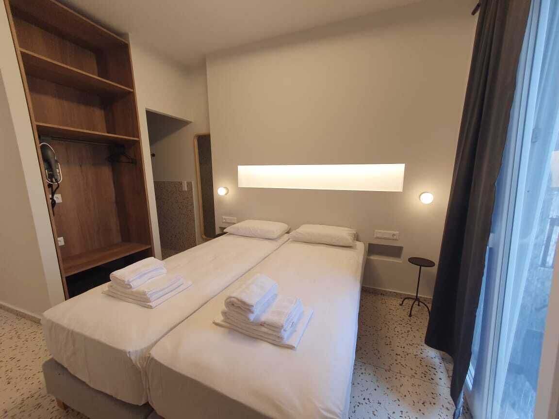 Habitación de hotel con cama doble, armario de madera, espejo, mesita de noche y ventana con cortinas.