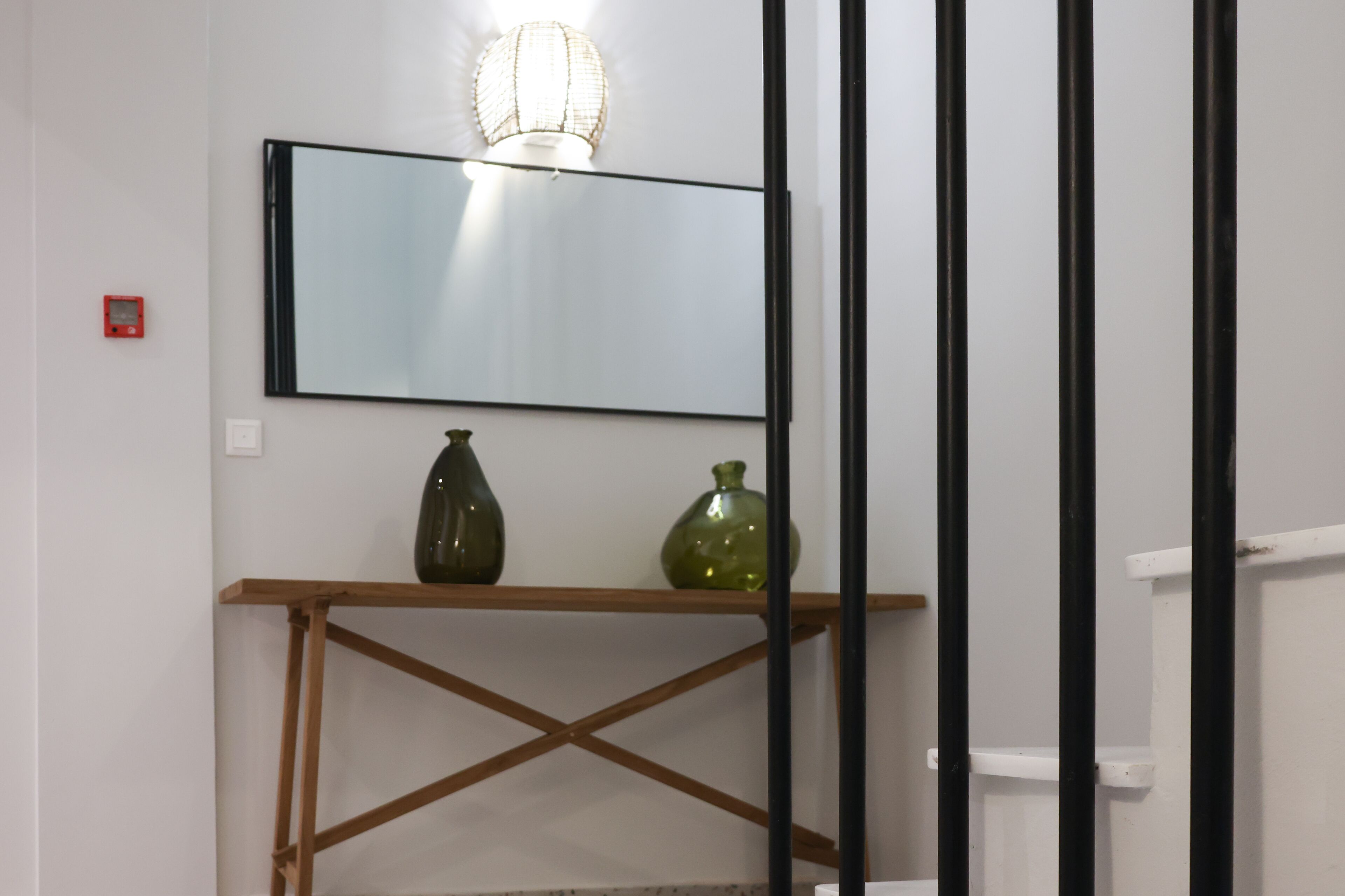 Quarto com mesa consola de madeira, dois vasos verdes, espelho fixado na parede e luminária.
