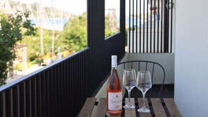 Ein Balkon mit einer Weinflasche und zwei Gläsern auf einem Holztisch, mit Blick auf eine Wohngegend.