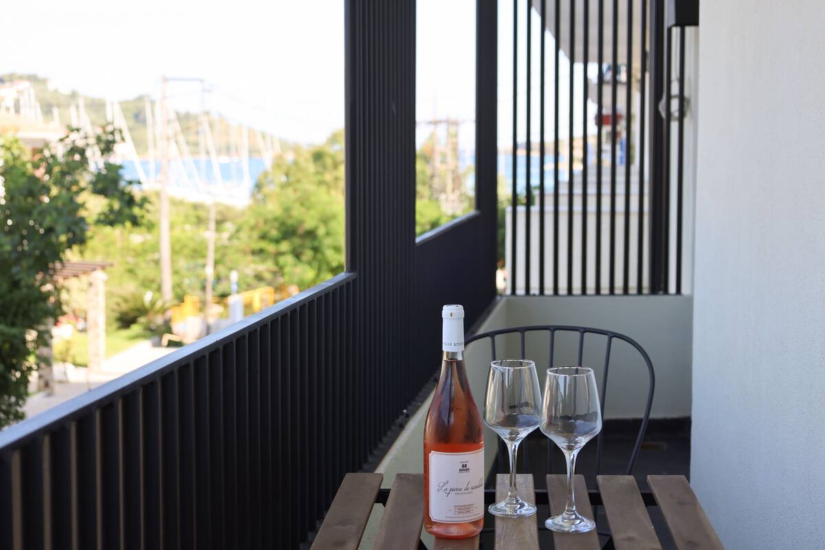 Een balkon met een fles wijn en twee glaasjes op een houten tafel, met uitzicht op een woongebied.