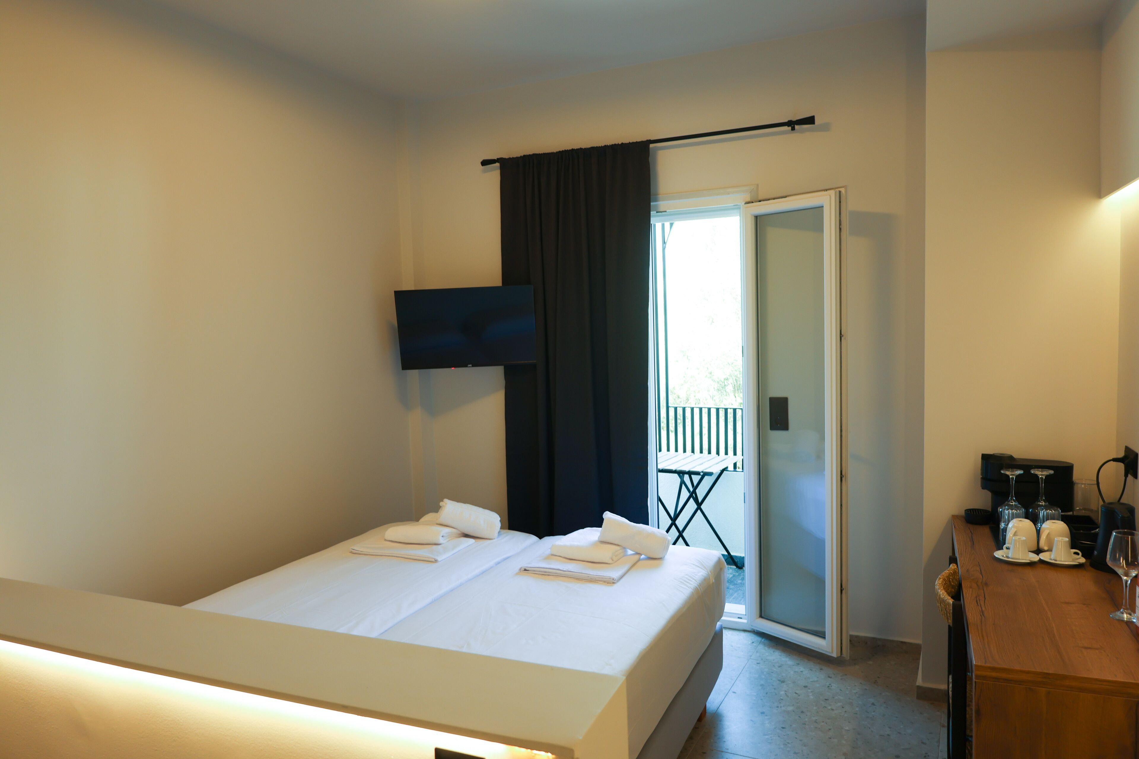 A hotel room with a bed, a TV, a coffee machine, and a table with glasses and cups.