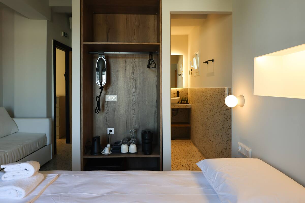 Hotelkamer met een bed, een kledingkast, een spiegel, een koffiezetapparaat en een wastafel in de badkamer.