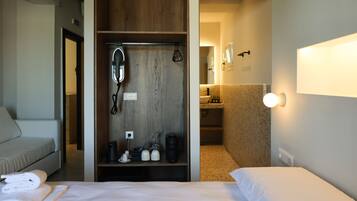 Una habitación de hotel con cama, armario, espejo, cafetera y lavamanos en el baño.