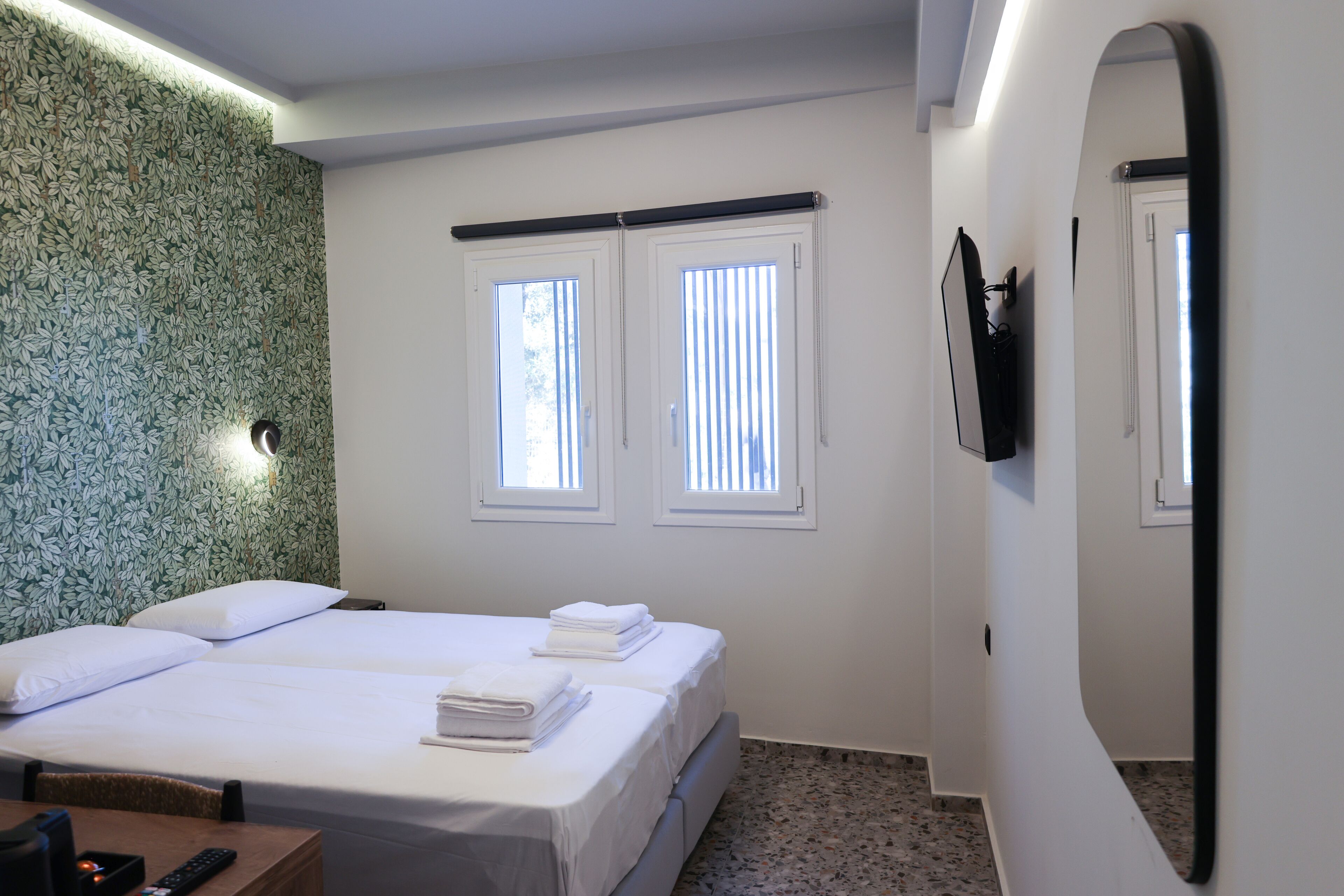 A hotel room with two beds, a TV mounted on the wall, and a window with blinds.