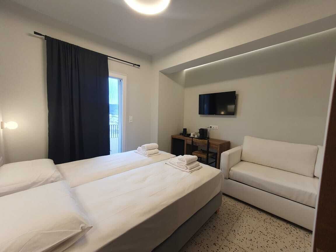 A hotel room with two beds, a sofa, a TV, and a desk.