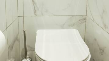 A bathroom with a white toilet, a bidet, and a wall-mounted flush handle.