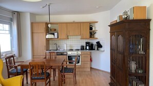 A modern kitchen with wooden cabinets, a dining table, chairs, a coffee maker, and a cabinet with glass doors. - Strandnahe 2-zimmer-fewo für 3 Personen mit Wlan (Graal-Müritz)