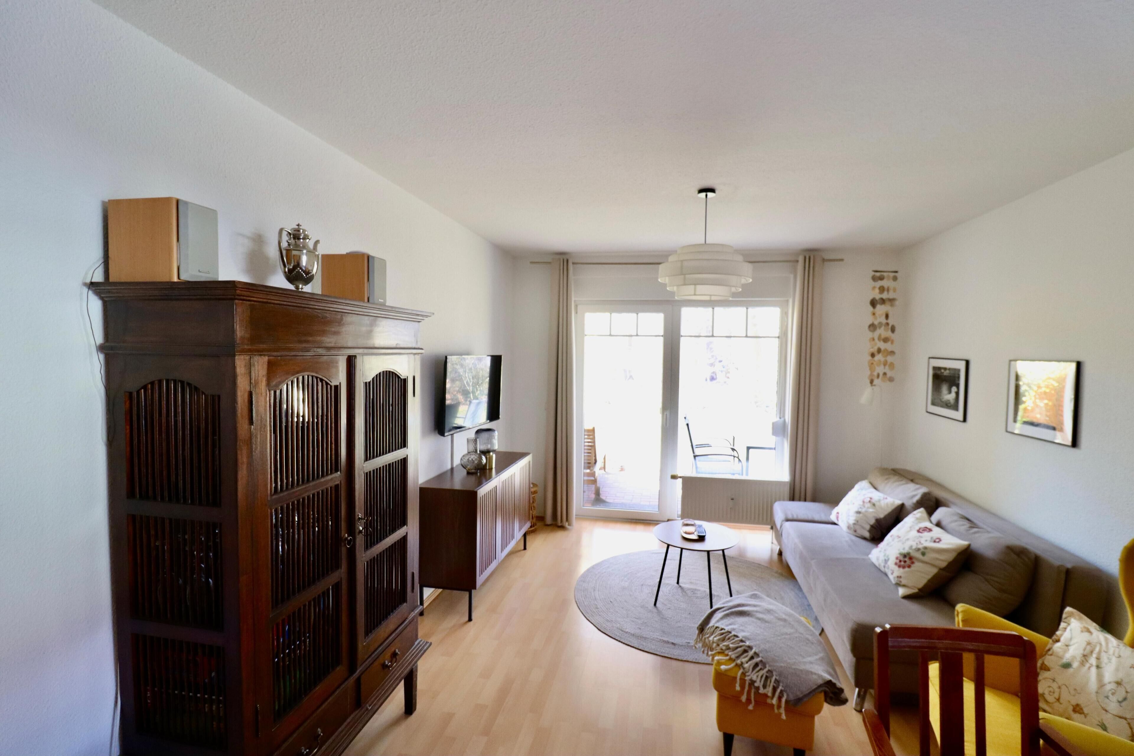Ein Wohnzimmer mit einer Couch, einem Holzschrank, einem Fernseher und einem Fenster.
