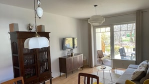 A living room with a wooden dining table, a sofa, a television, and a large window. - Strandnahe 2-zimmer-fewo für 3 Personen mit Wlan (Graal-Müritz)