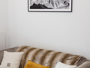 Ein Wohnzimmer mit einer Couch, einer Decke und einem gerahmten Bild an der Wand.