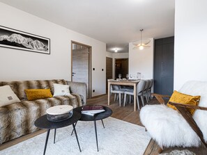 Ein modernes Wohnzimmer mit einer Couch, einem Couchtisch, einem Esstisch mit Stühlen und einem flauschigen weißen Sessel.