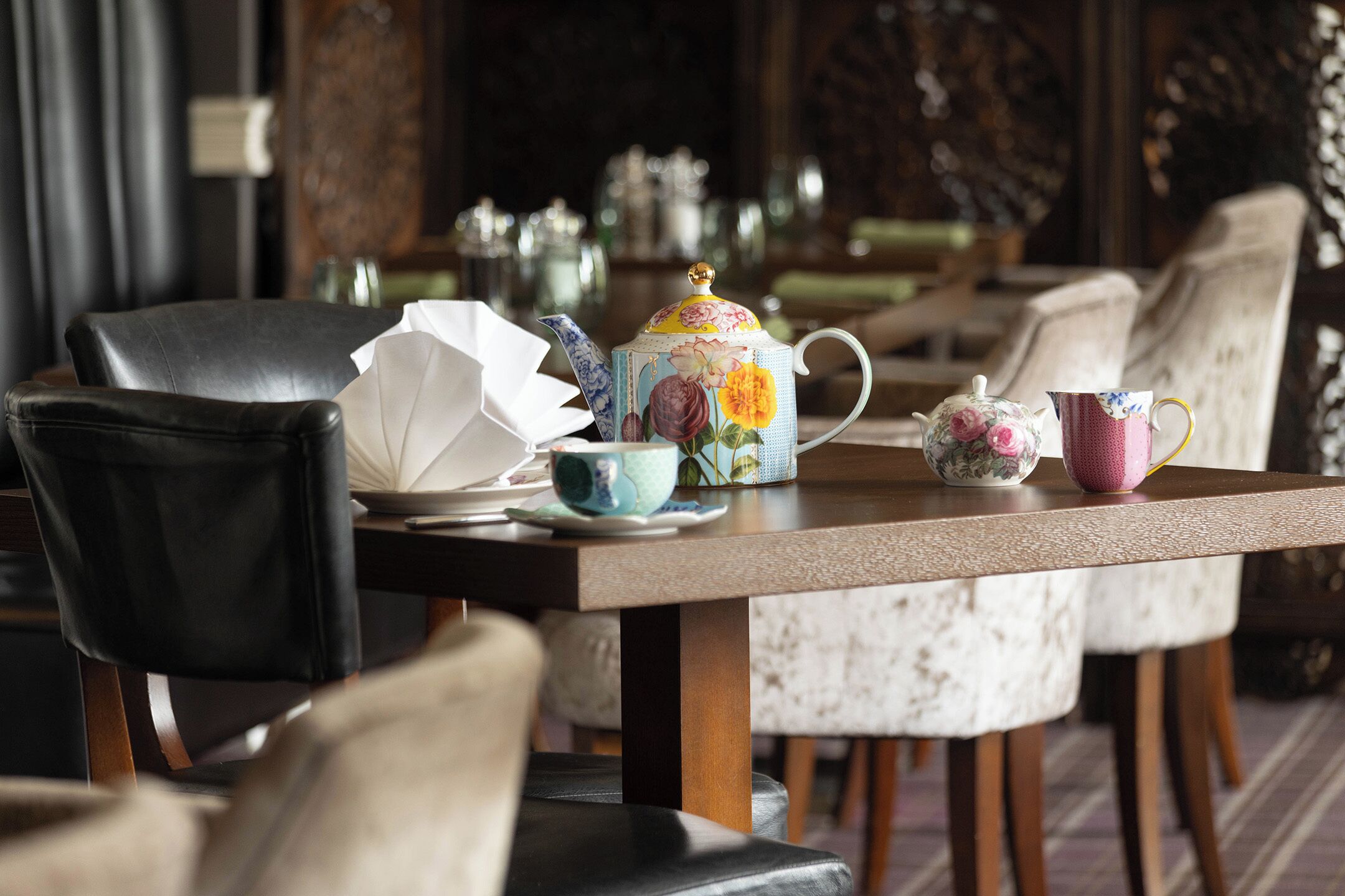 A dining table with a floral teapot, a pink cup, and a white teacup.