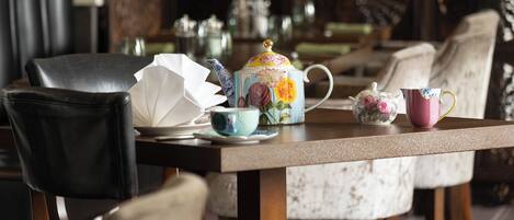 A dining table with a floral teapot, a pink cup, and a white teacup.