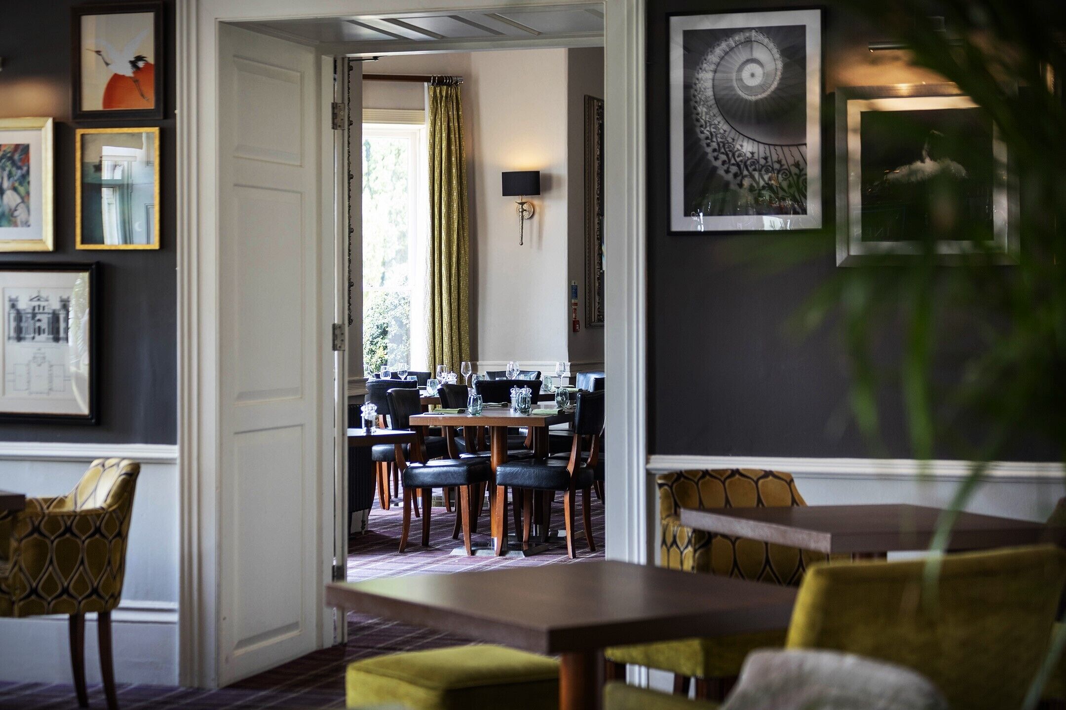 A dining area with tables and chairs, framed artwork on the walls, and a view into another room.