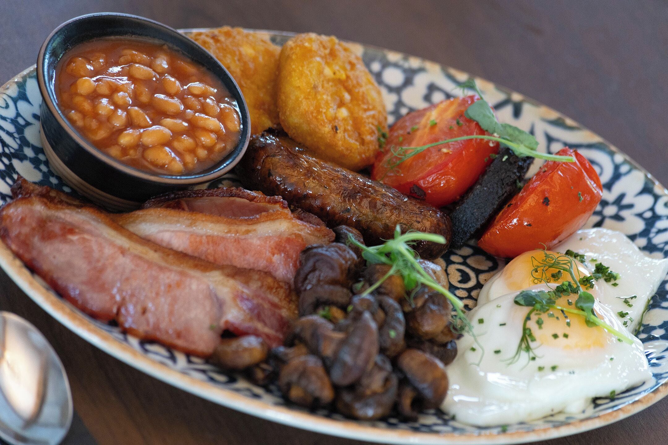 Un plato de comida para el desayuno con frijoles, tocino, salchichas, huevos y tomates.