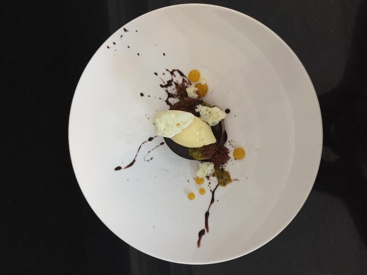 A dessert on a white plate with chocolate sauce, a scoop of ice cream, and some garnishes.