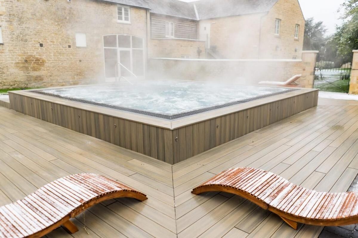 A hot tub with steam rising, surrounded by wooden deck and lounge chairs.