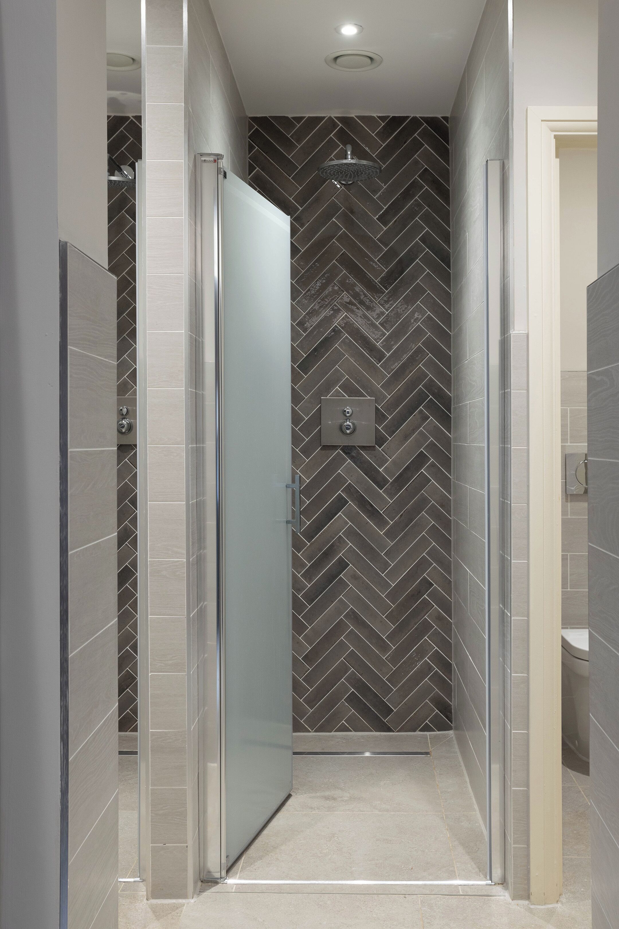 Une salle de bain moderne avec une douche à parois de verre, un mur orné d’un motif en chevrons et des toilettes visibles sur la droite.