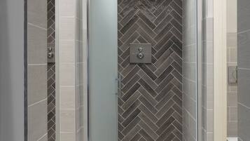Une salle de bain moderne avec une douche à parois de verre, un mur orné d’un motif en chevrons et des toilettes visibles sur la droite.
