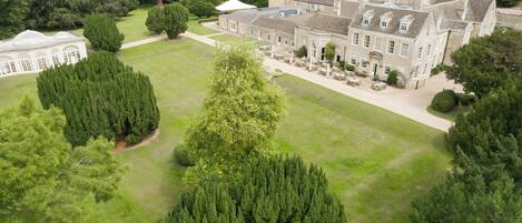 A large estate with a central lawn, surrounded by mature trees and a historic building with multiple windows and a covered patio area.