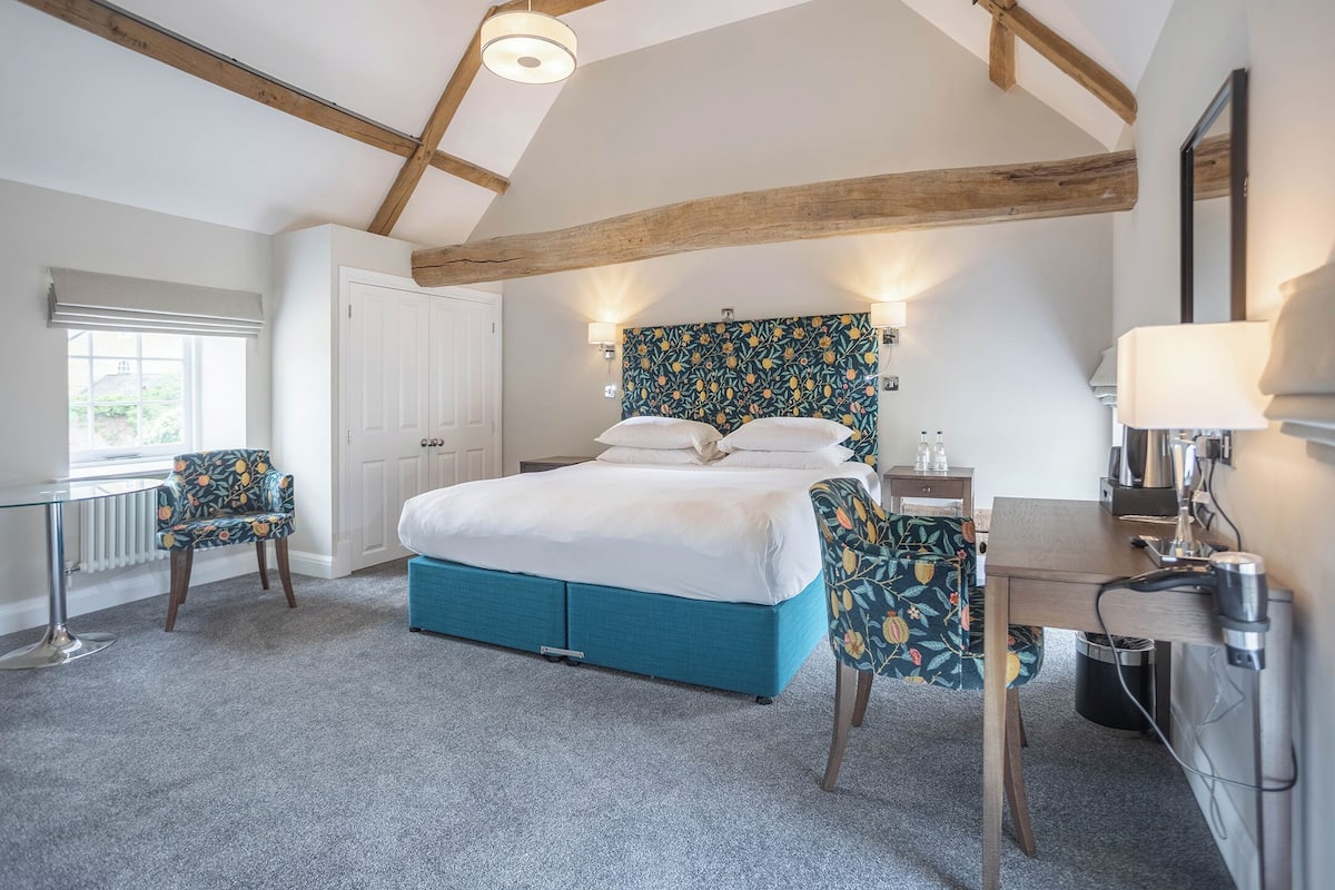 A bedroom with a bed, two chairs, a desk, and a radiator.
