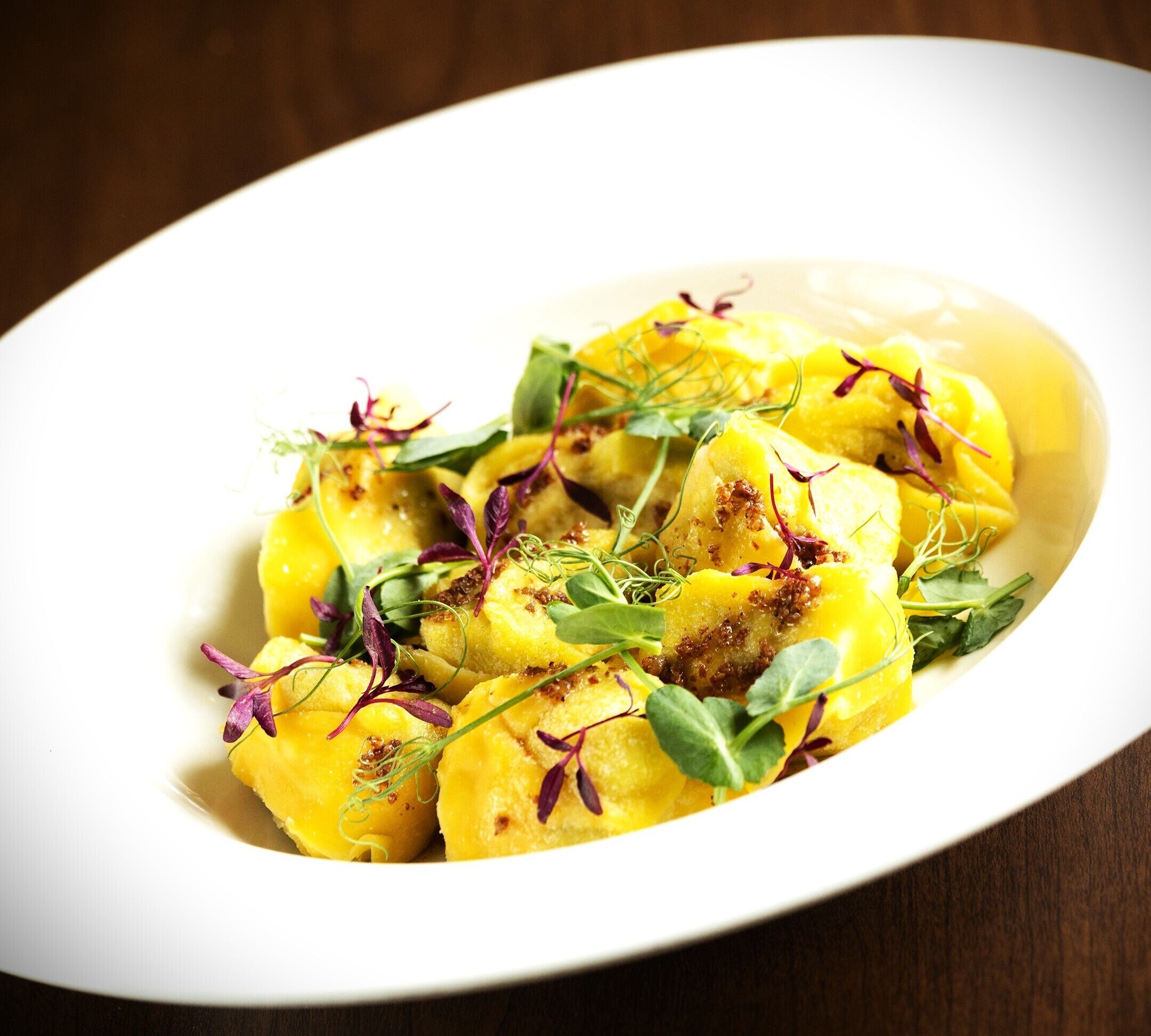 A white oval plate with a dish of yellow food garnished with purple and green herbs.