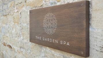 A wooden sign with a floral design and the text "The Garden Spa" mounted on a stone wall.