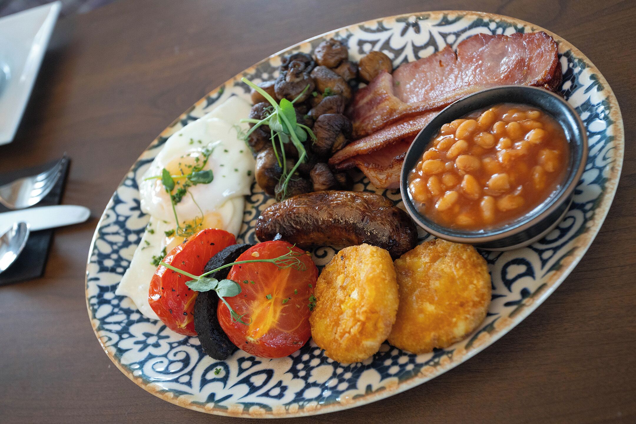A plate of food with eggs, bacon, mushrooms, beans, tomatoes, and sausages.