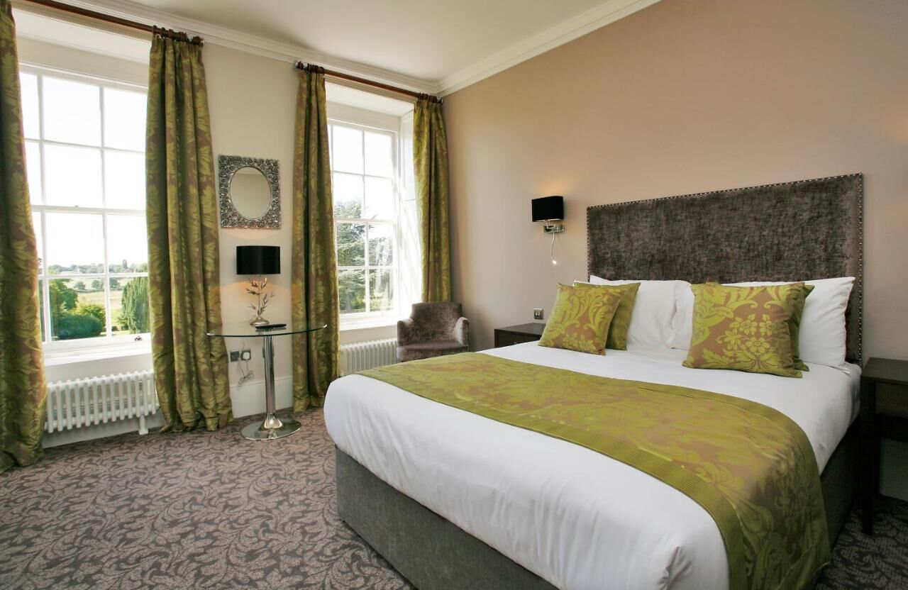 A hotel room with a large bed, a small table, a chair, and a view of the outdoors through a window.