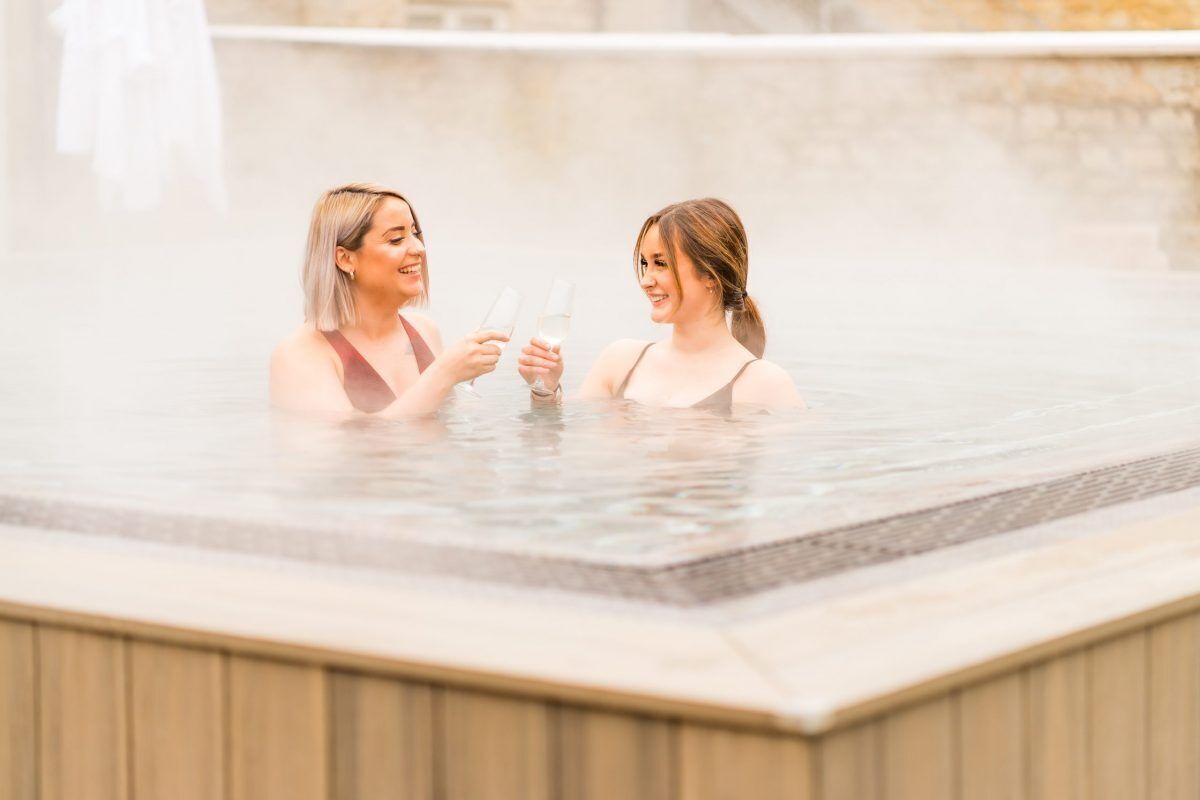 To personer i jacuzzi med stenvæg i baggrunden.